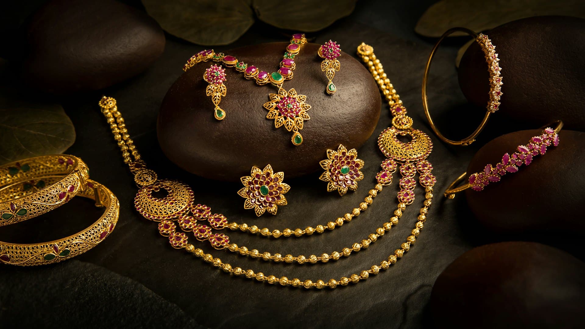 Indian gold necklace, earrings and bangles displayed on dark stones