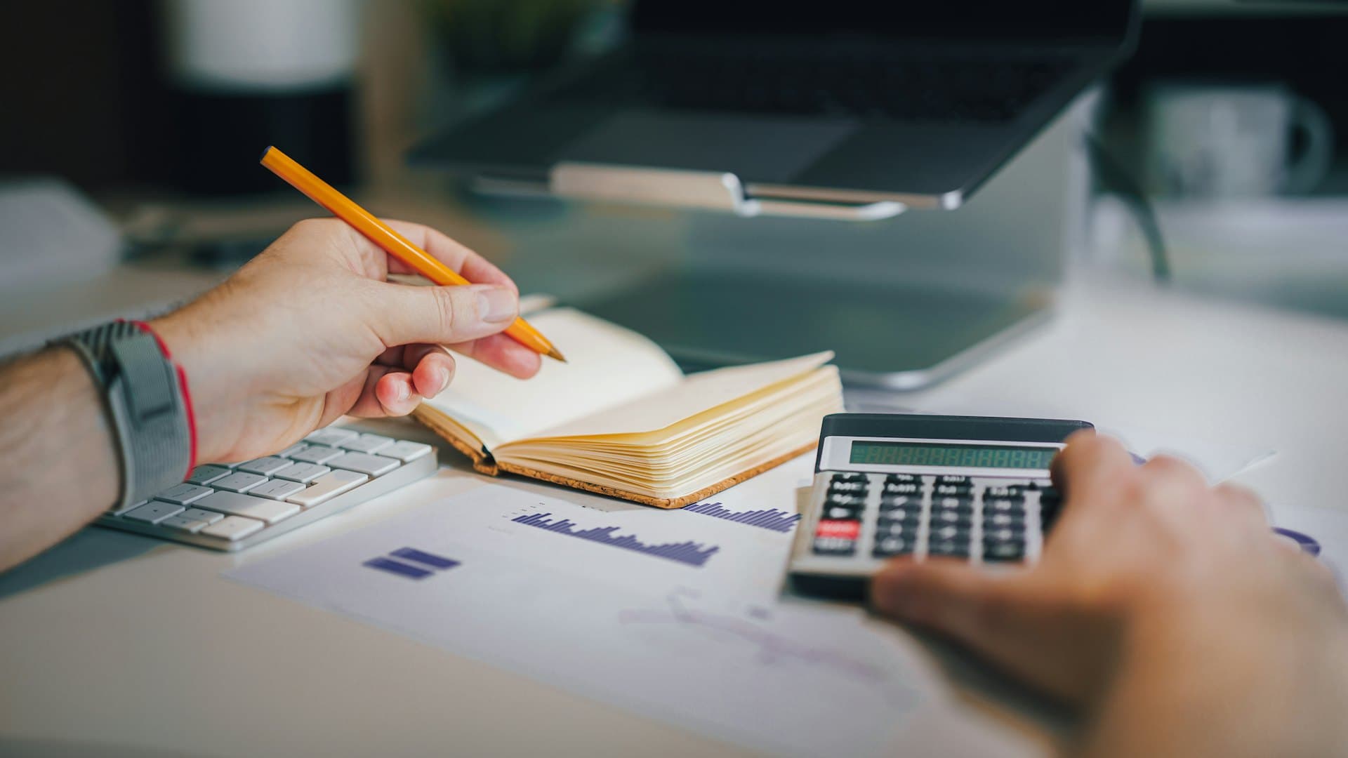 Accountant working with a calculator, notebook and financial charts at a desk